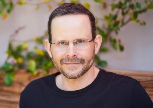 Confident man with glasses smiling indoors, natural background, inspirational and engaging portrait.